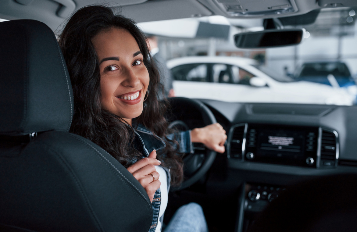 Mujer viendo hacia atrás sonriendo mientras conduce un automóvil