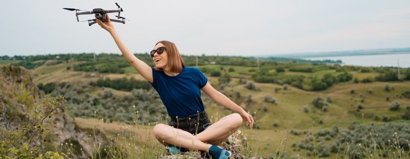 Mujer sentada en  una colina sosteniendo un dron con su mano derecha
